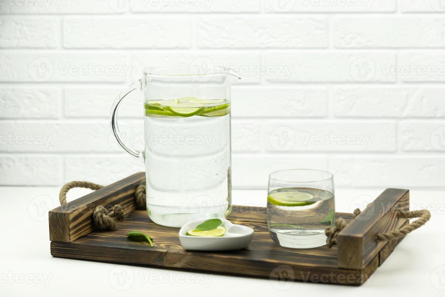 A home made lemonade made of lime stands in a glass and jug on a wooden tray photo