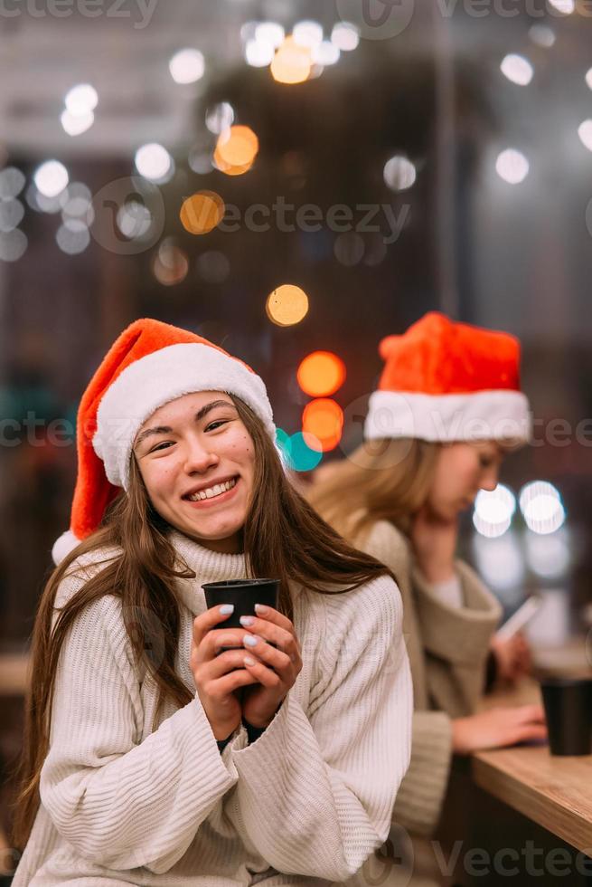 Girl wearing Santa hat sitting in coffee shop and drinking coffee photo