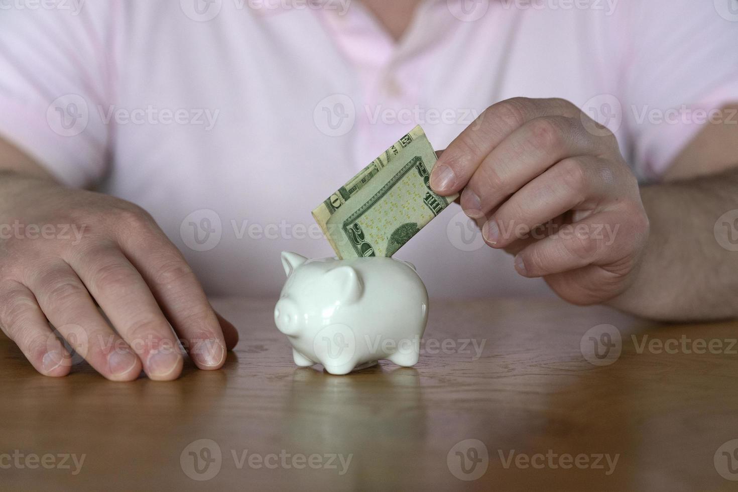 A man puts a dollar banknote into a piggybank for saving purposes photo