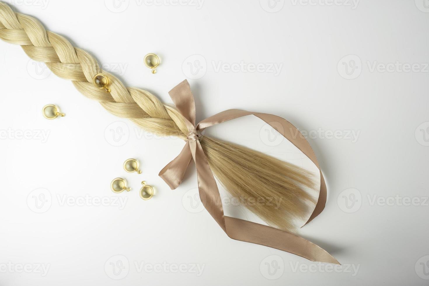 A natural oil or serum for hair care treatment and a tress of blonde hair with bow lying on a white background photo