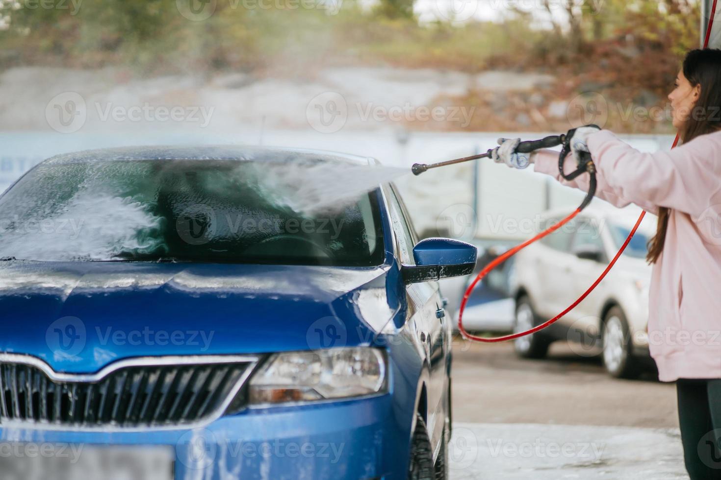 Young woman washing blue car at car wash photo