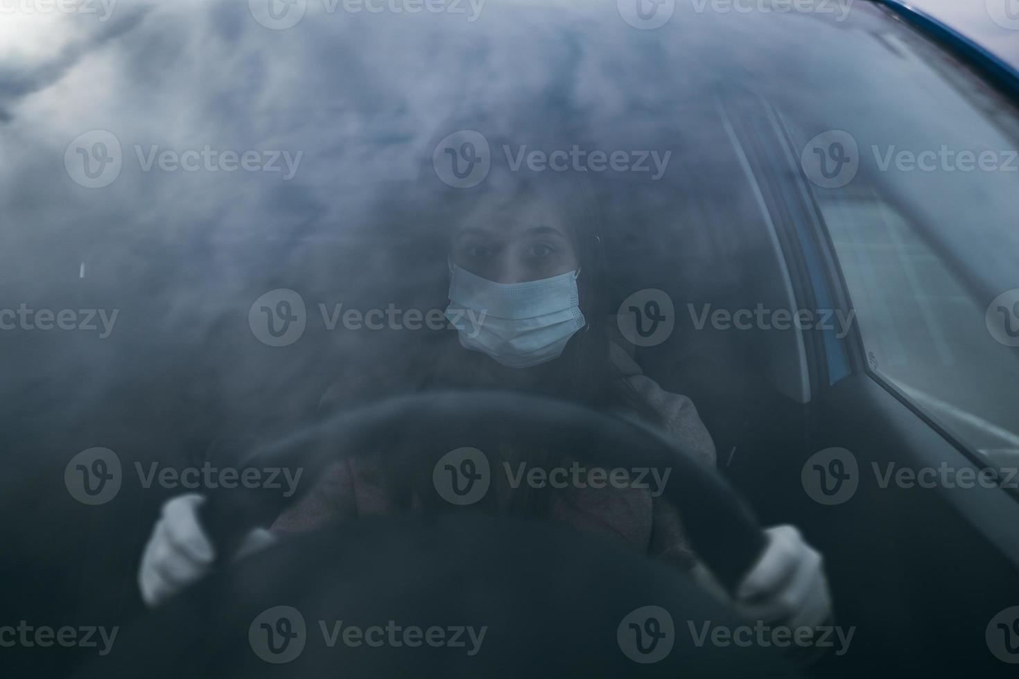 Young woman in a mask and gloves driving a car. photo