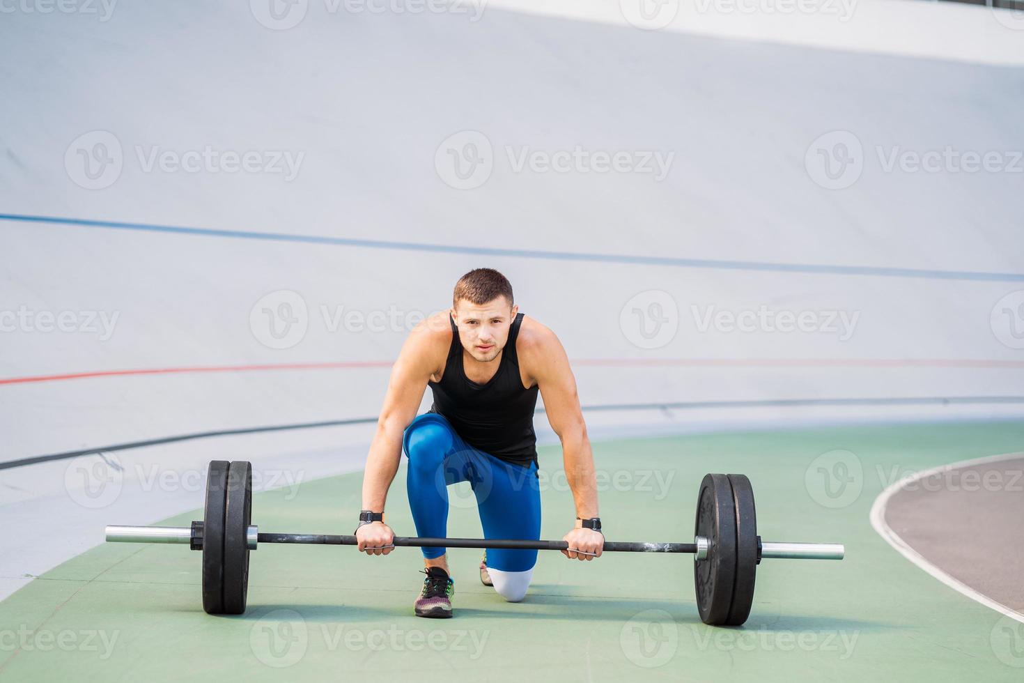 Young guy raises the bar in the stadium, outdoor workout photo