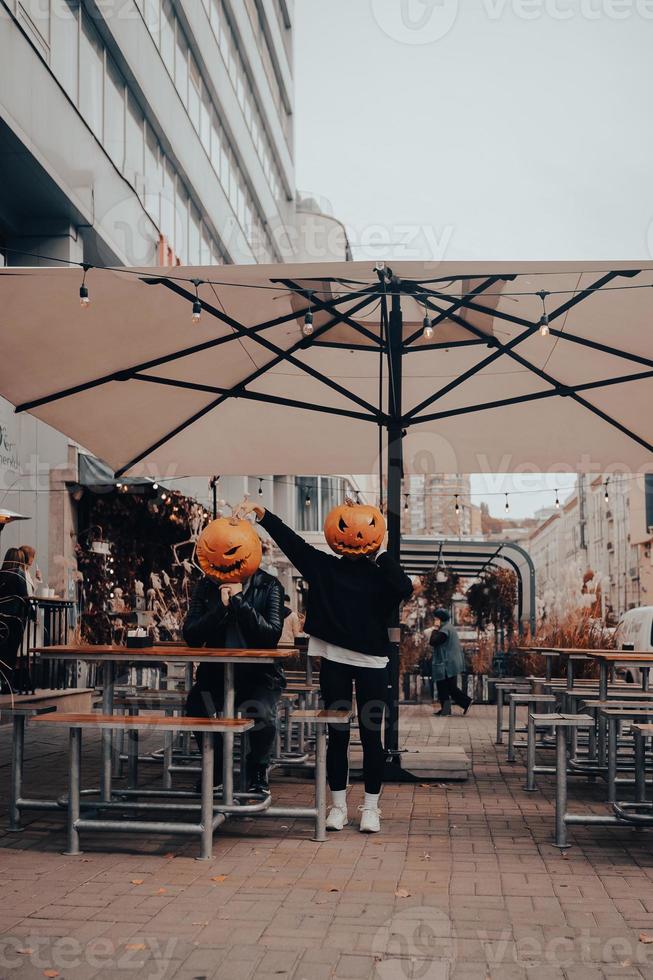 chico y chica con cabezas de calabaza en un café de la calle foto