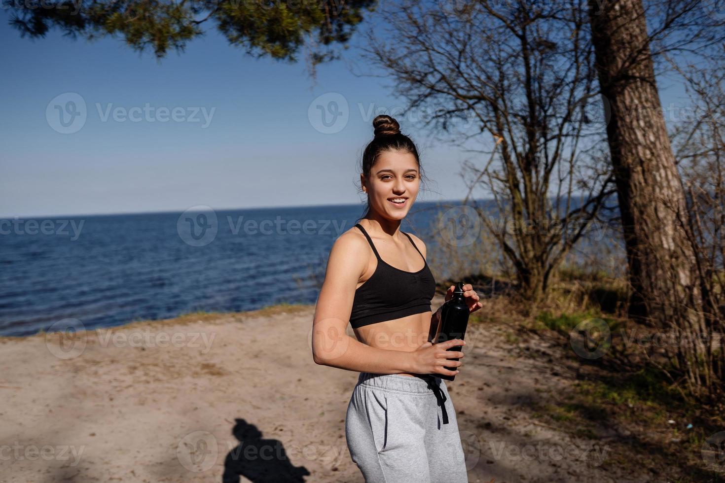Slim young woman drinking water after training photo