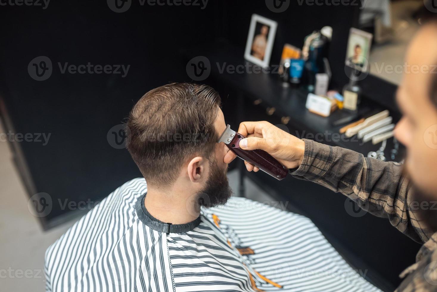 Master in barbershop makes men's haircutting with hair clipper photo