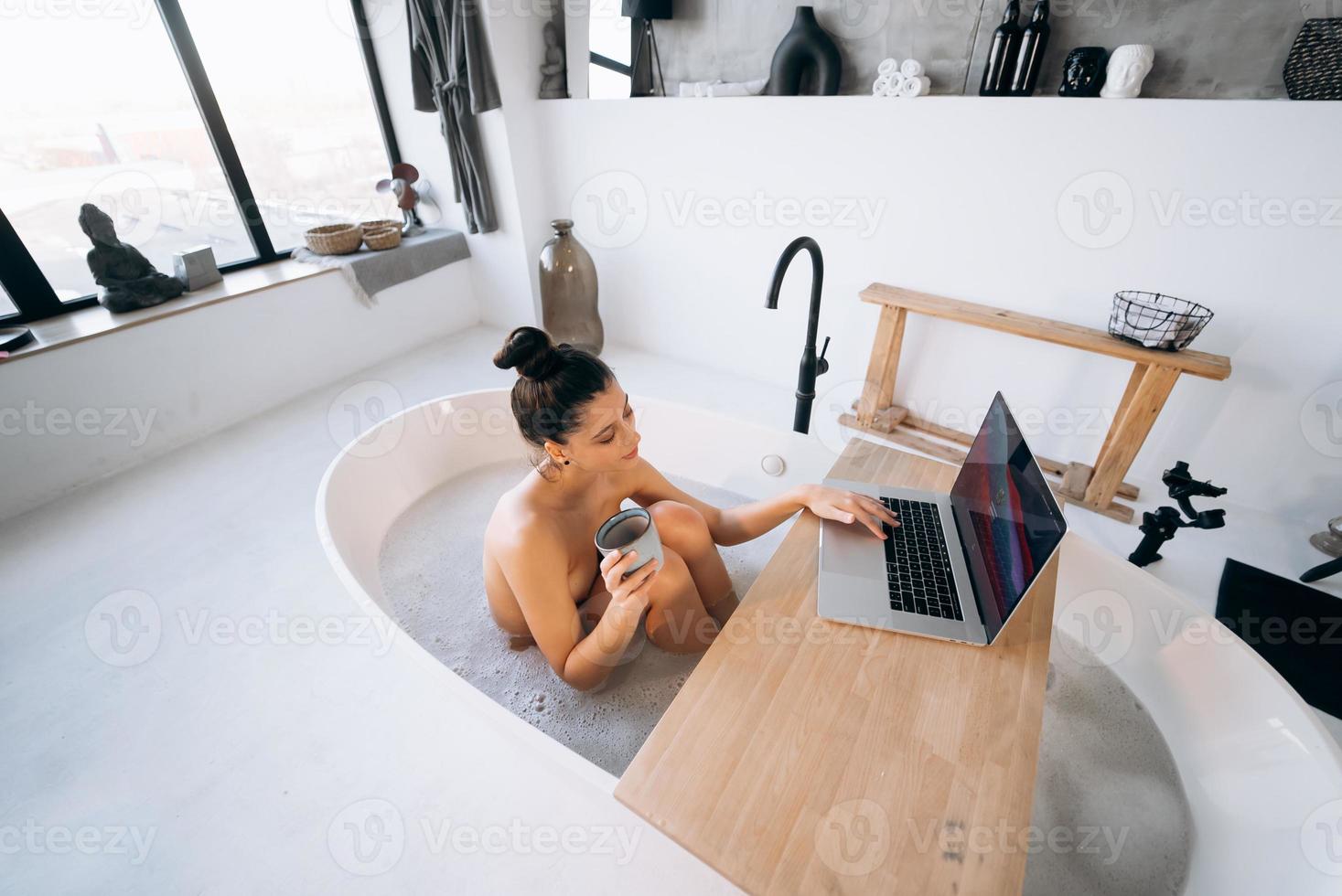 Young woman working on laptop while taking a bathtub photo
