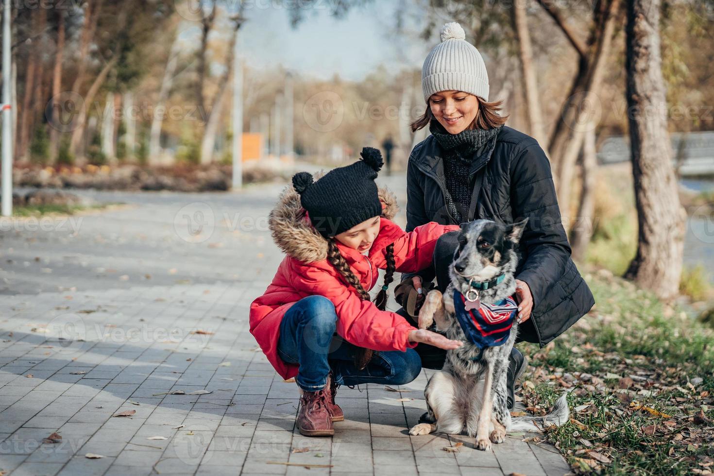 Happy mother and her daughter playing with dog in autumn park photo