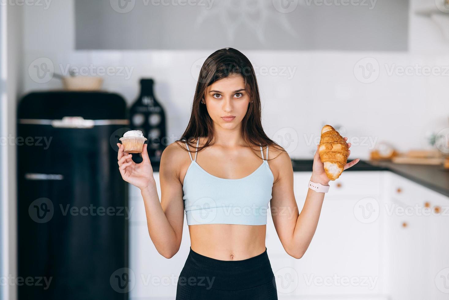 A young woman holds a croissant and a cake in her hands. photo