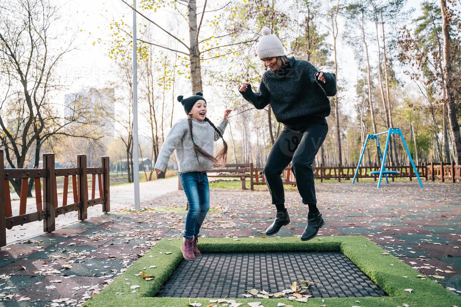 Mom and her daughter jumping together on trampoline in autumn park photo