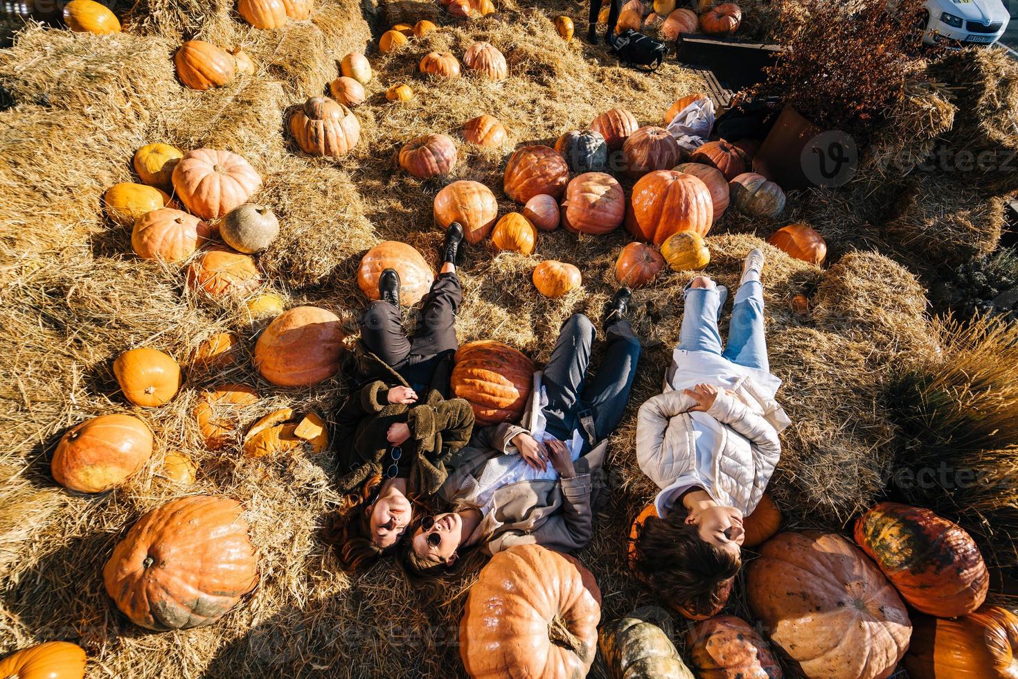 Young girls lie on haystacks among pumpkins. View from above photo