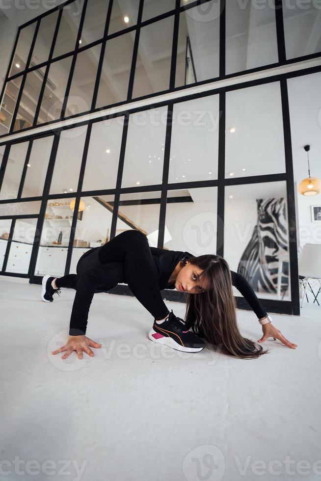 mujer joven con traje deportivo negro haciendo pose de yoga en el interior. foto