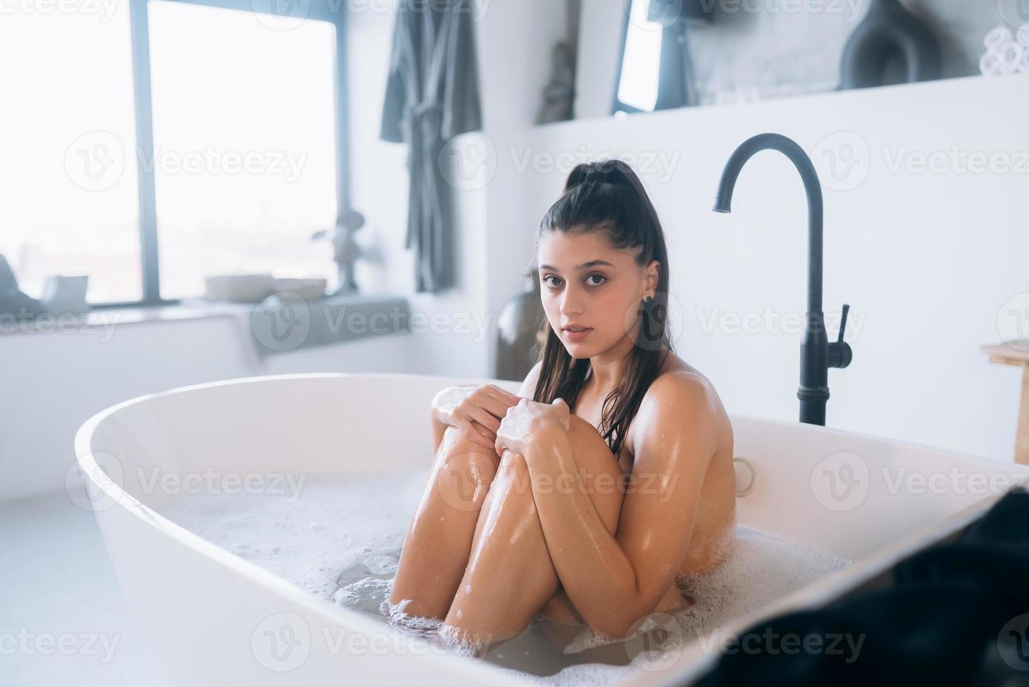 Young woman hugs her legs while sitting in the bath photo