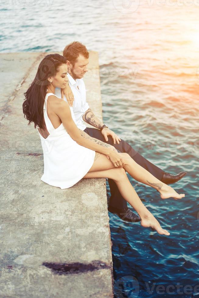 Young couple are sitting on the pier by the sea photo