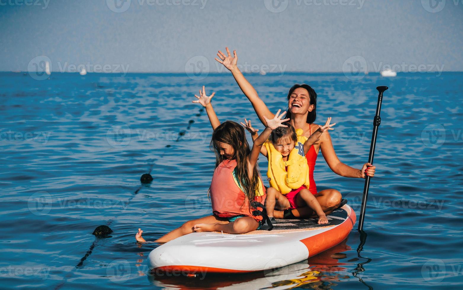 Mother with two daughters stand up on a paddle board photo