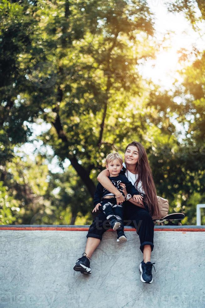 bella joven hipster mamá e hijo pequeño en el skatepark foto