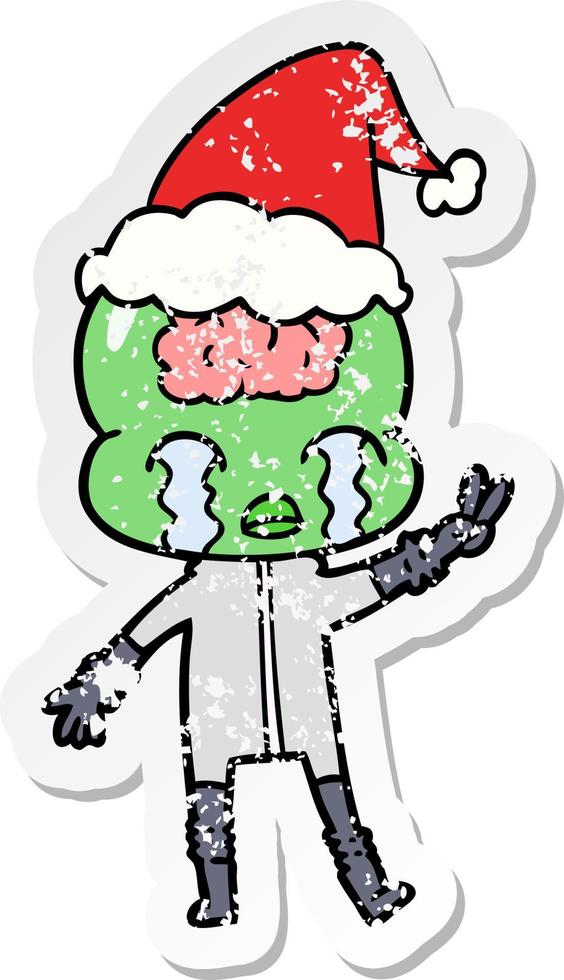 distressed sticker cartoon of a big brain alien crying and giving peace sign wearing santa hat vector