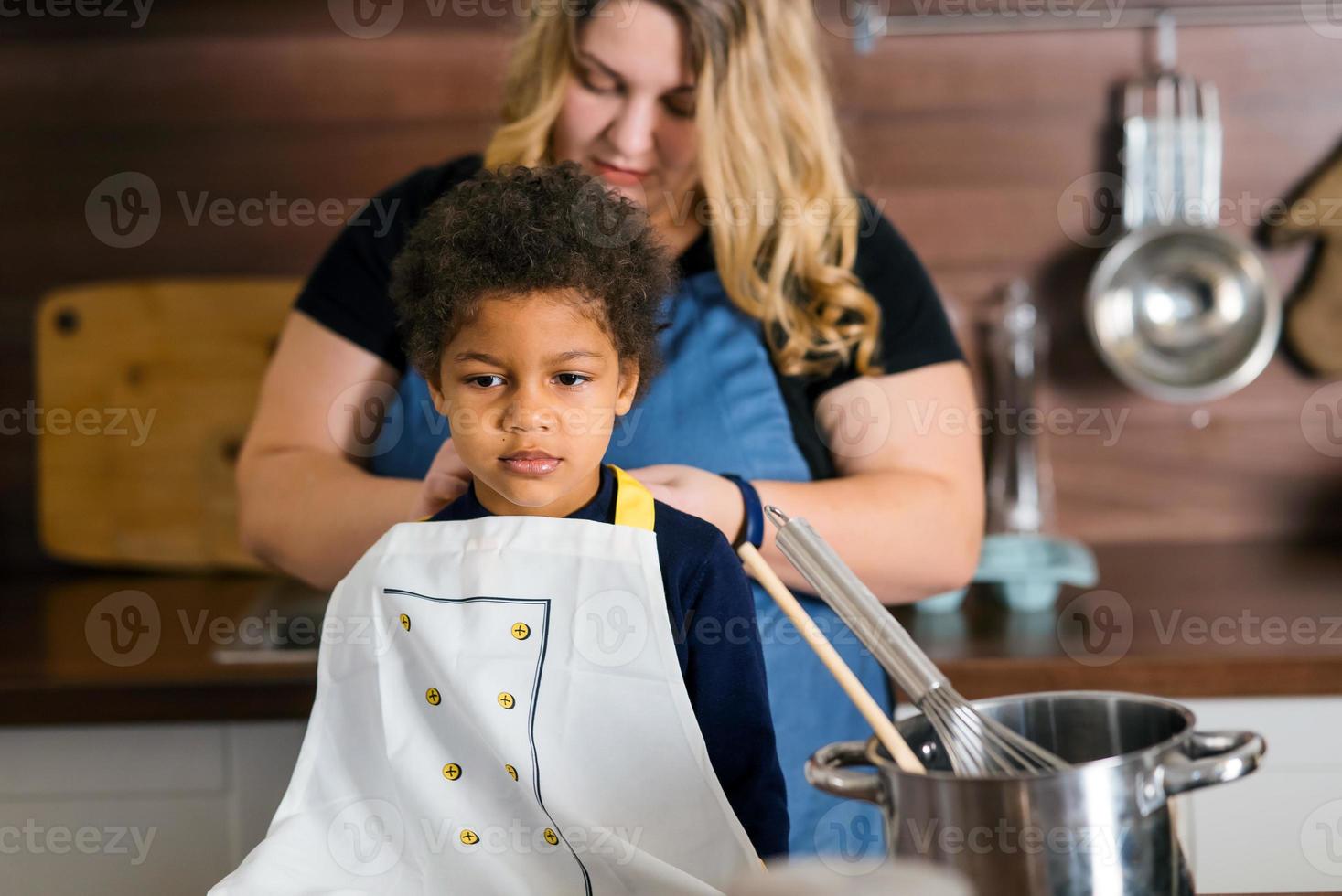 Mom ties an apron to her daughter in the kitchen photo