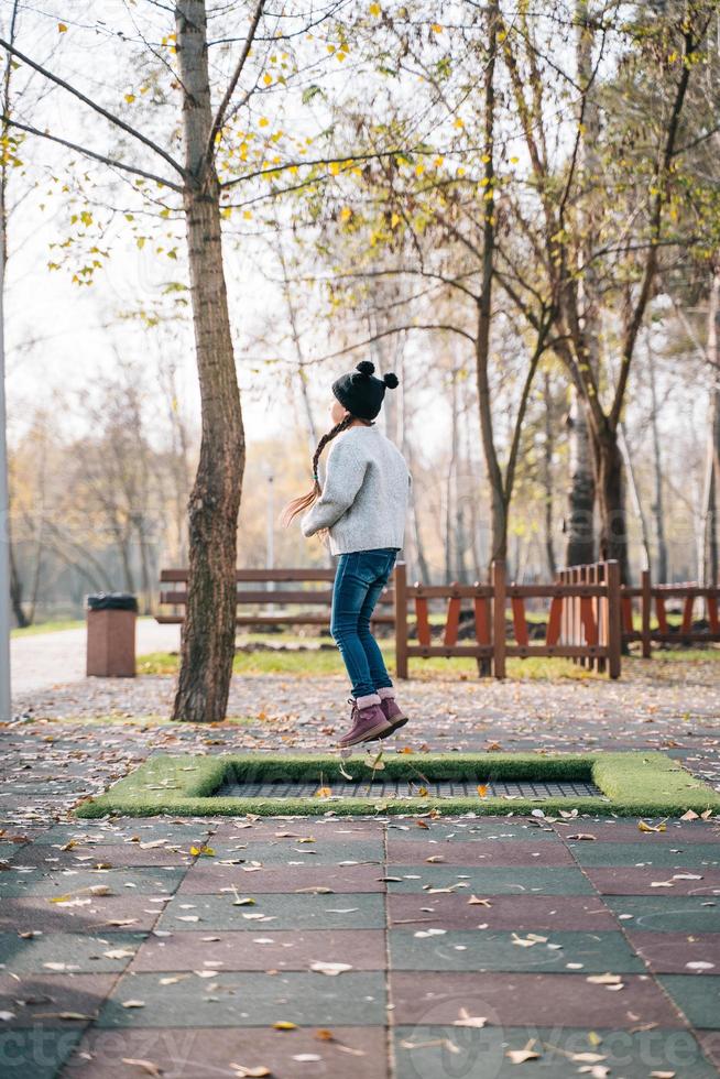 Happy school girl jumping on a small trampoline in the park photo
