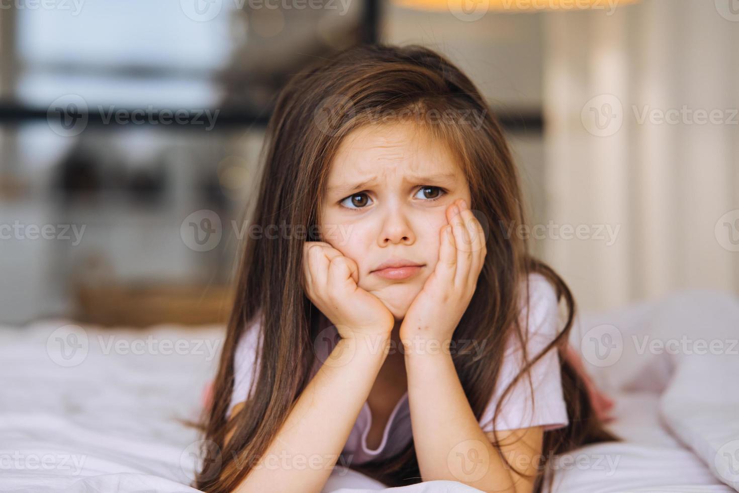 linda niña con una cara triste acostada en la cama foto