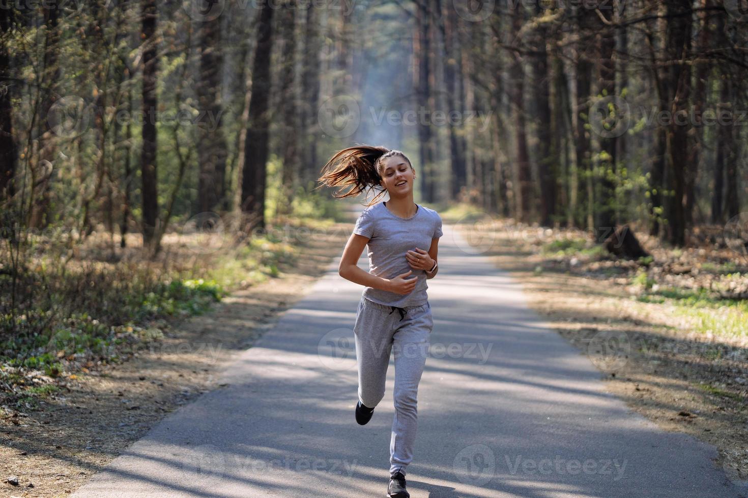 Beautiful young woman running in green park on sunny summer day photo
