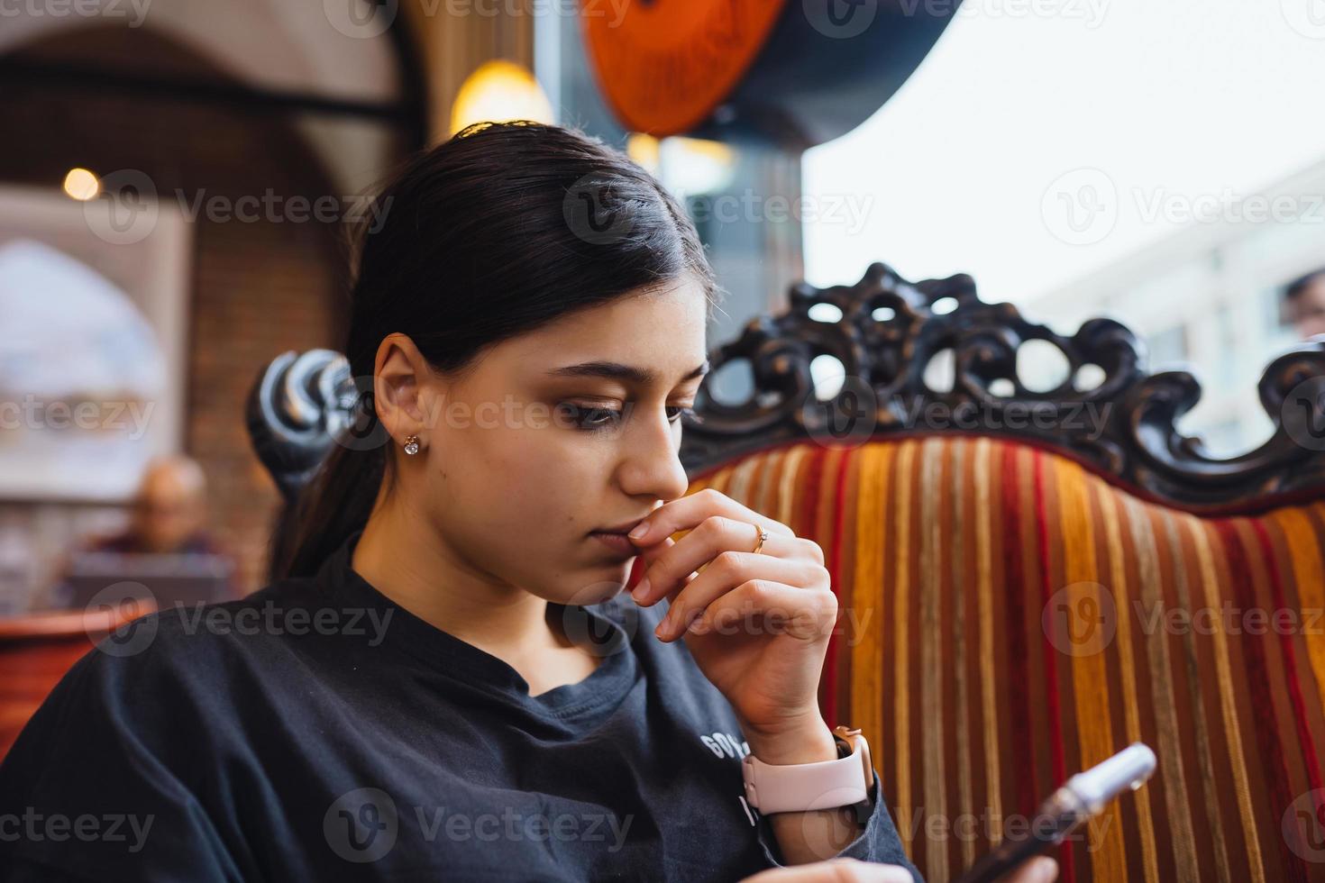 Pretty young girl resting on a big soft chair in a cafe, chatting on the phone photo