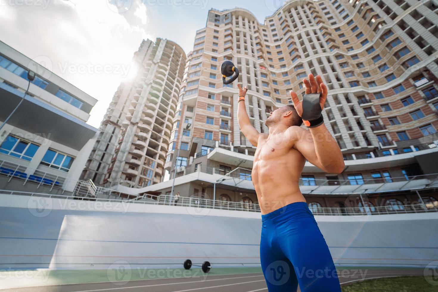 Sportive guy training with kettlebell on the background of a tall building. photo