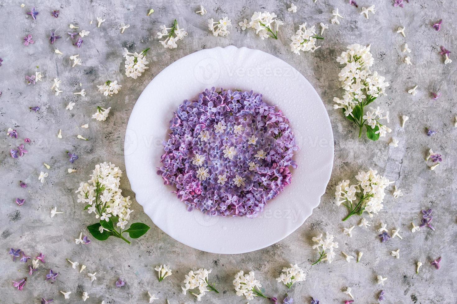 Served plate with purple and white lilac flowers on gray concrete background, top view. Spring season concept with minimal design. photo