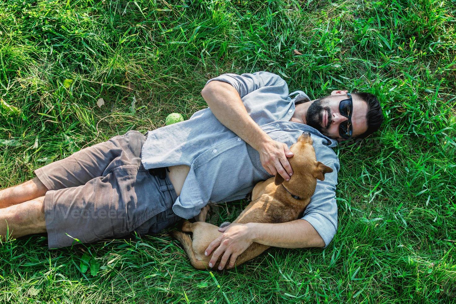 Top view of man and dog lying on green grass. Attractive European man is hugging his dog. photo