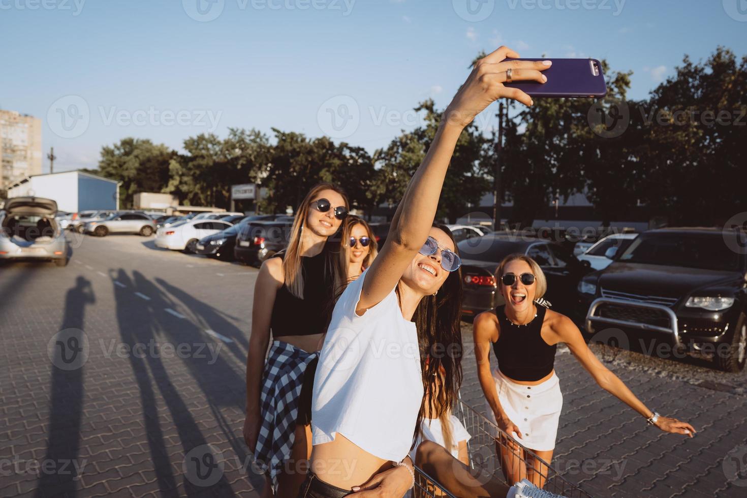 cinco chicas jóvenes se divierten con un carrito de supermercado en un aparcamiento foto