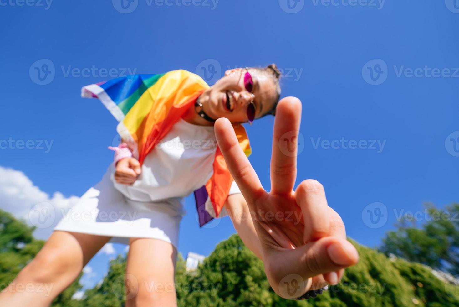 una mujer joven desarrolla una bandera del arco iris contra el cielo foto