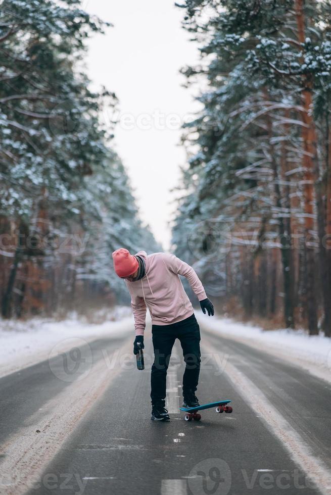 Skateboarder standing on the road in the middle of the forest, surrounded by snow photo