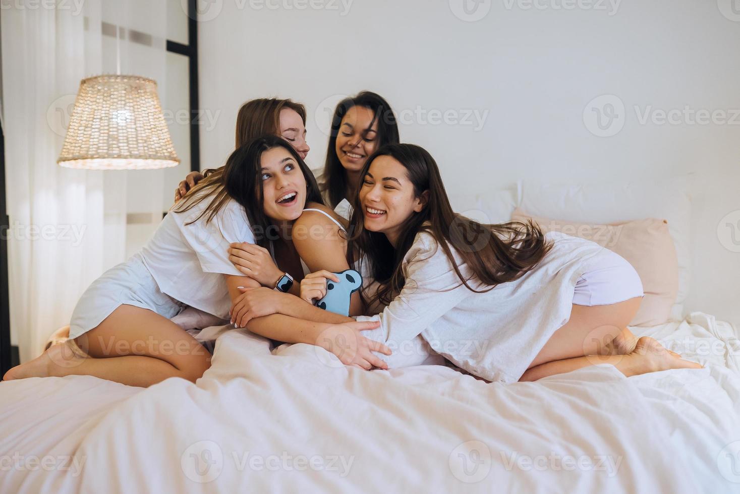 Positive young girls women friends indoors on bed at the hen party at home. photo