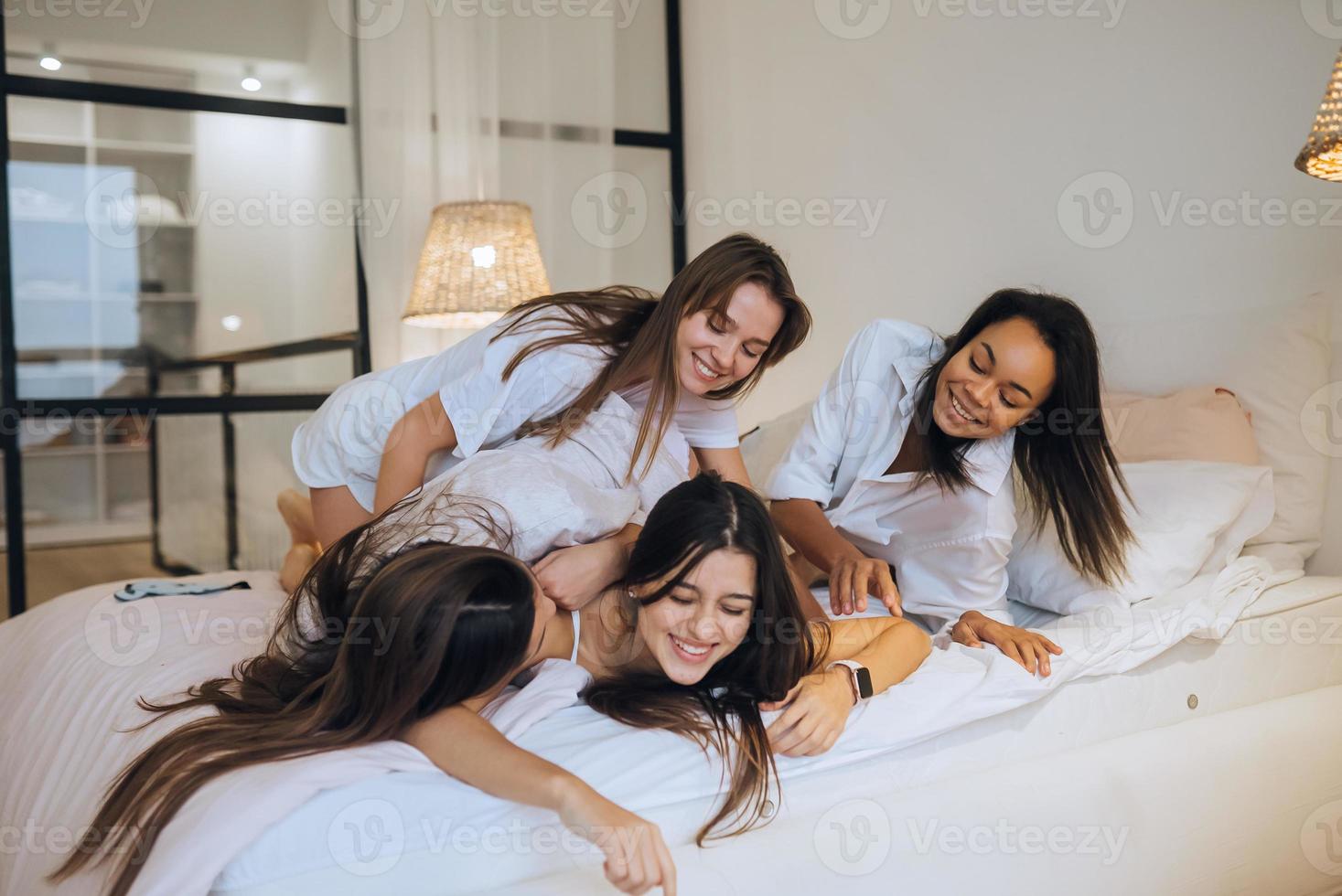 Positive young girls women friends indoors on bed at the hen party at home. photo