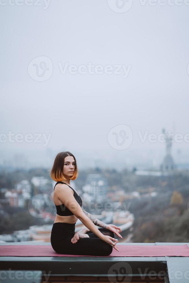 Woman practicing yoga on the mat on the roof and doing yoga exercises photo