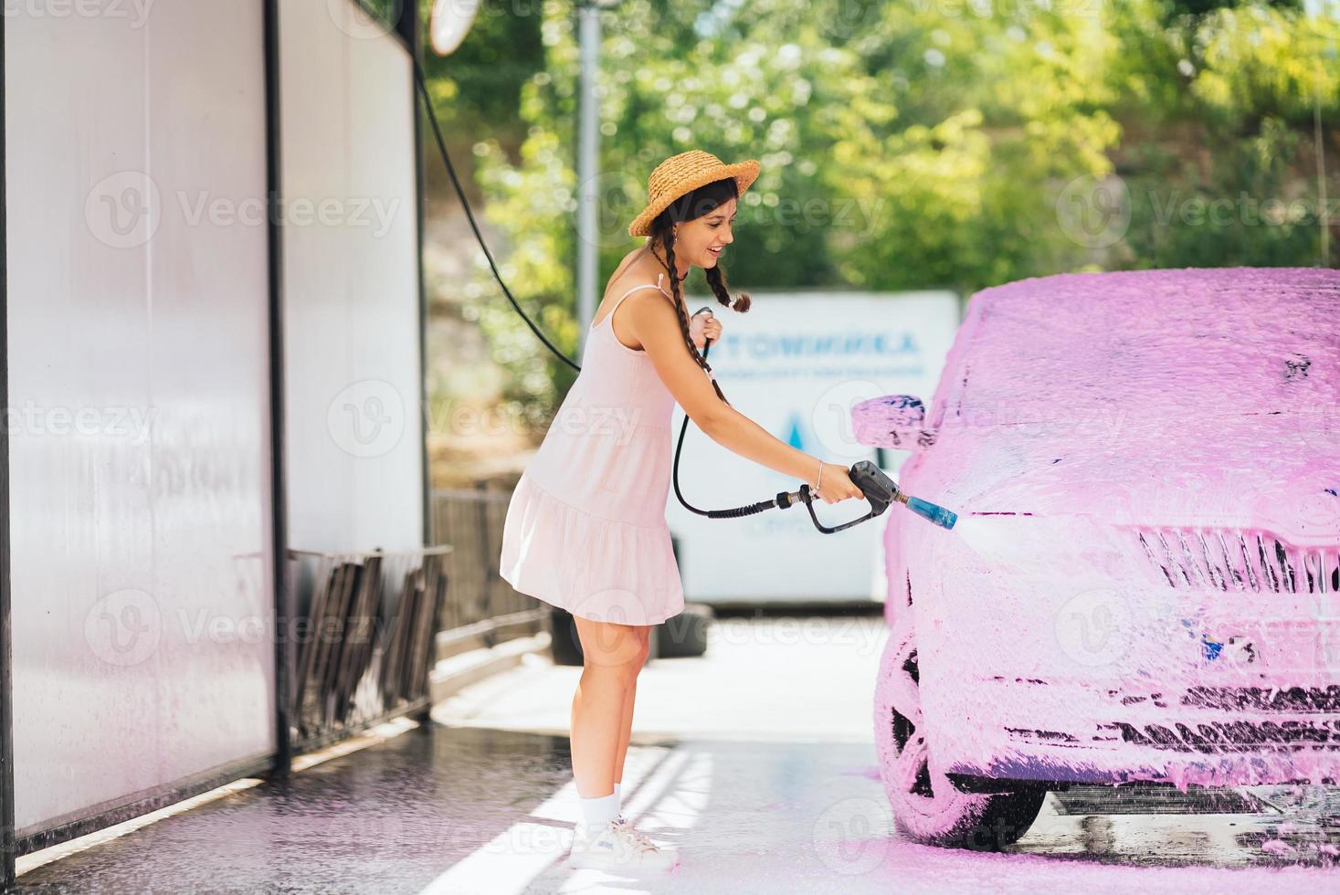 Brunette from a high-pressure hose applies a cleaner on the car photo