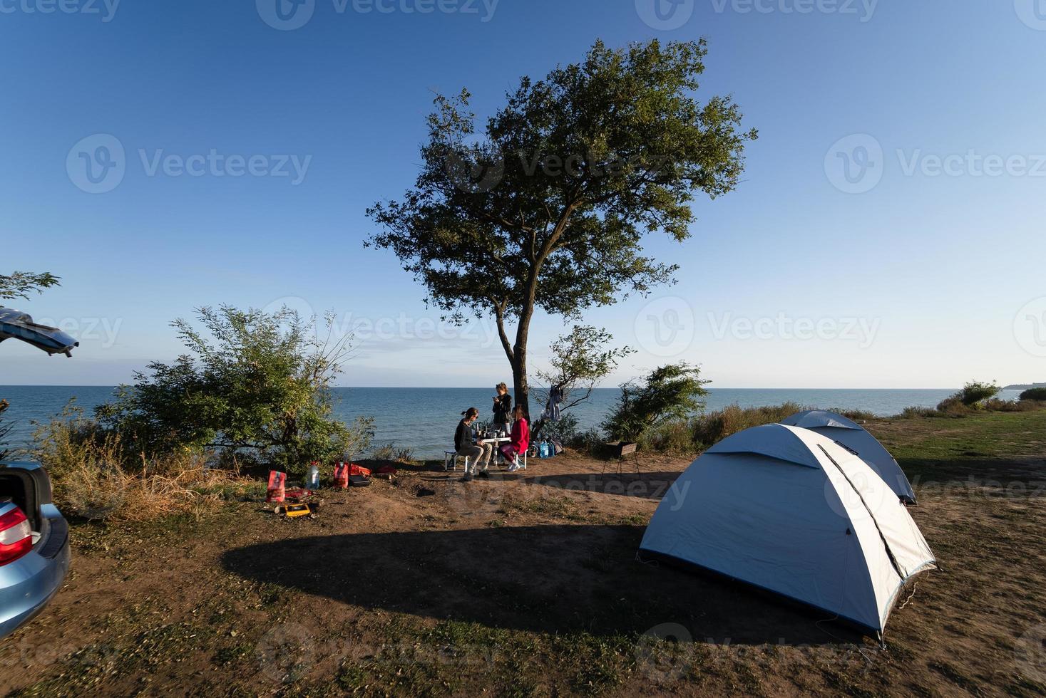 concepto de amistad, ocio y comida rápida - grupo de amigos felices comiendo en la playa en verano foto