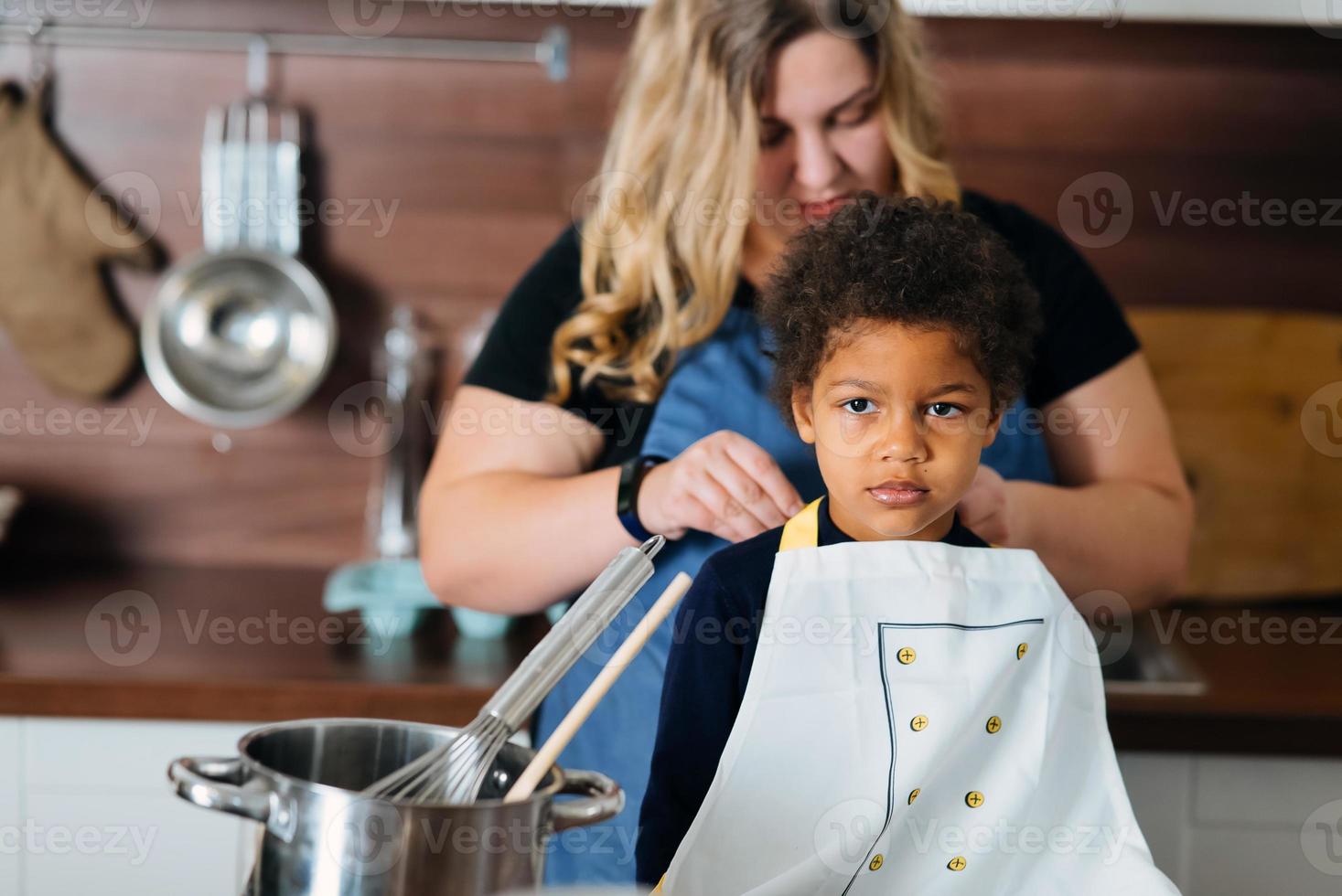 Mom ties an apron to her daughter in the kitchen photo