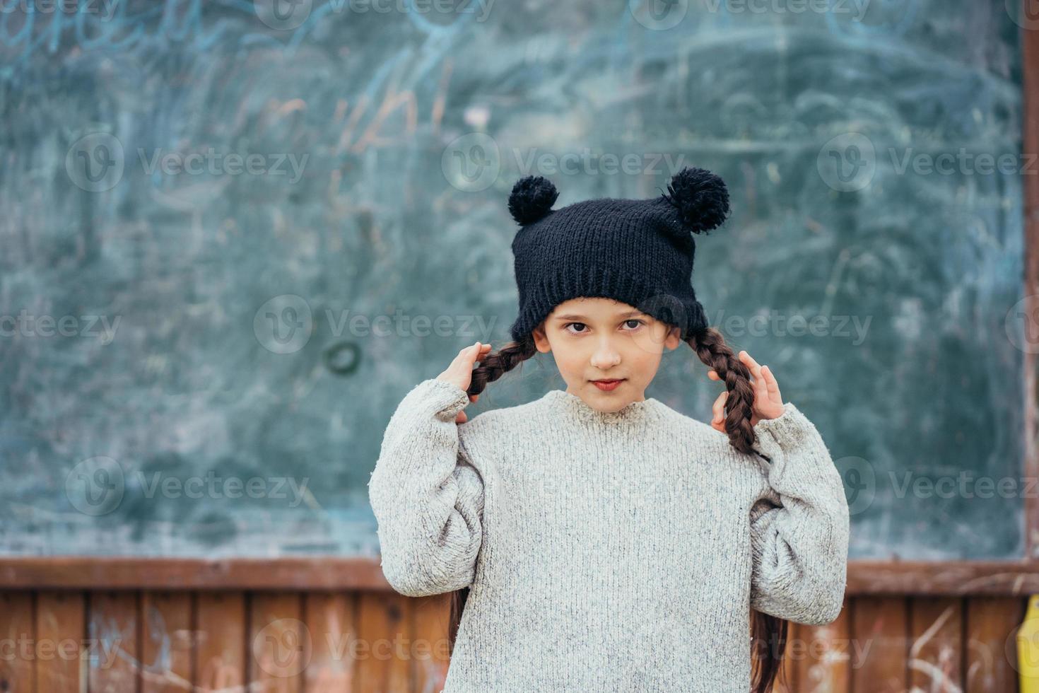 Little girl in a hat posing on the background of the school blackboard photo
