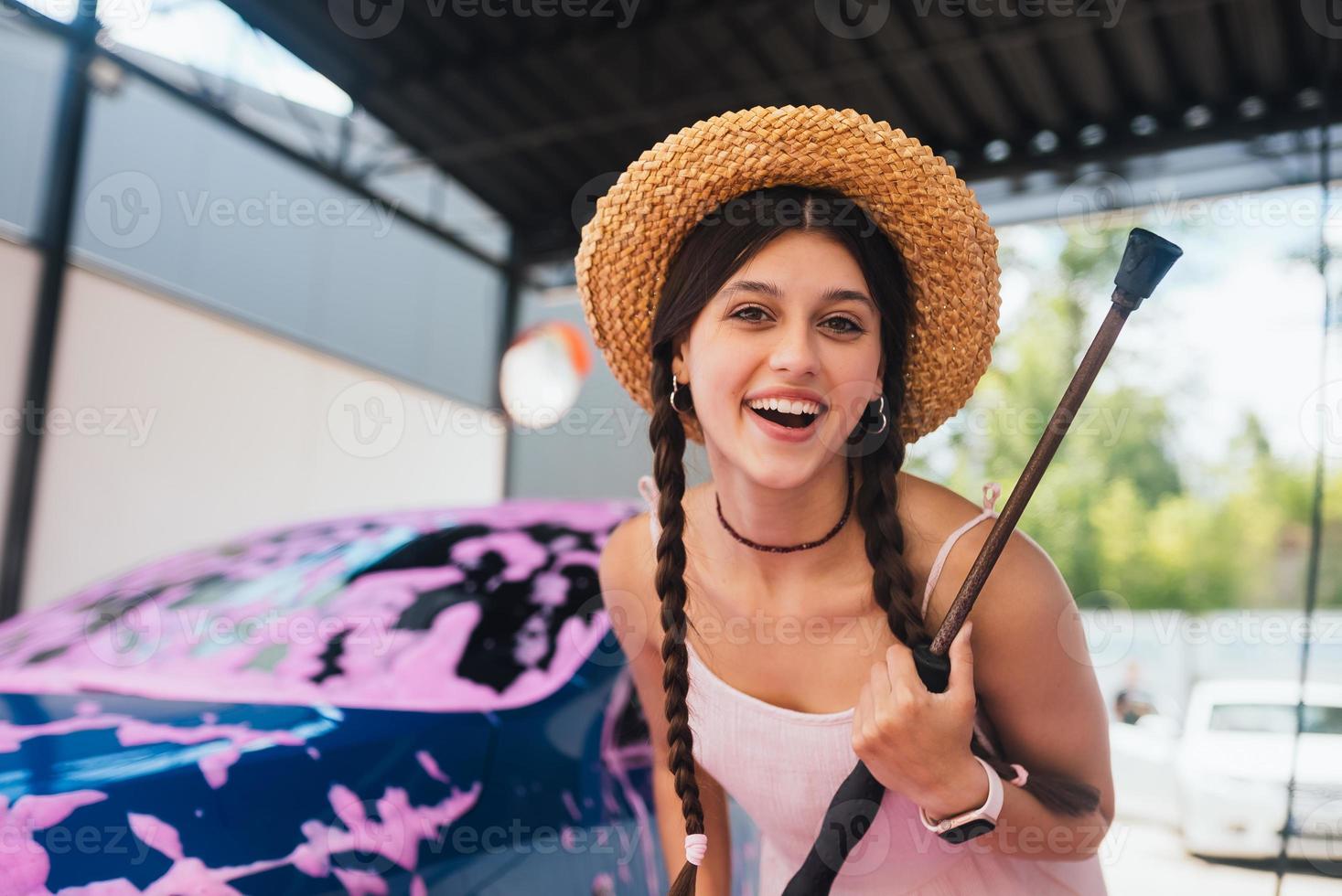 Woman with hose stands by car covered in pink foam photo