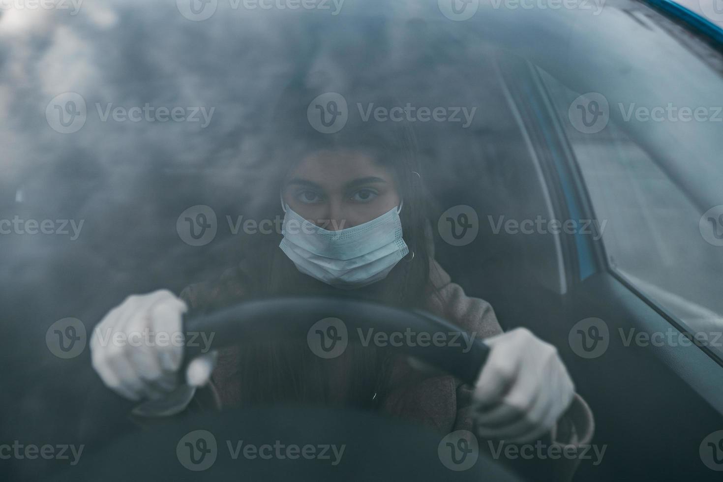 mujer joven con una máscara y guantes conduciendo un automóvil. foto