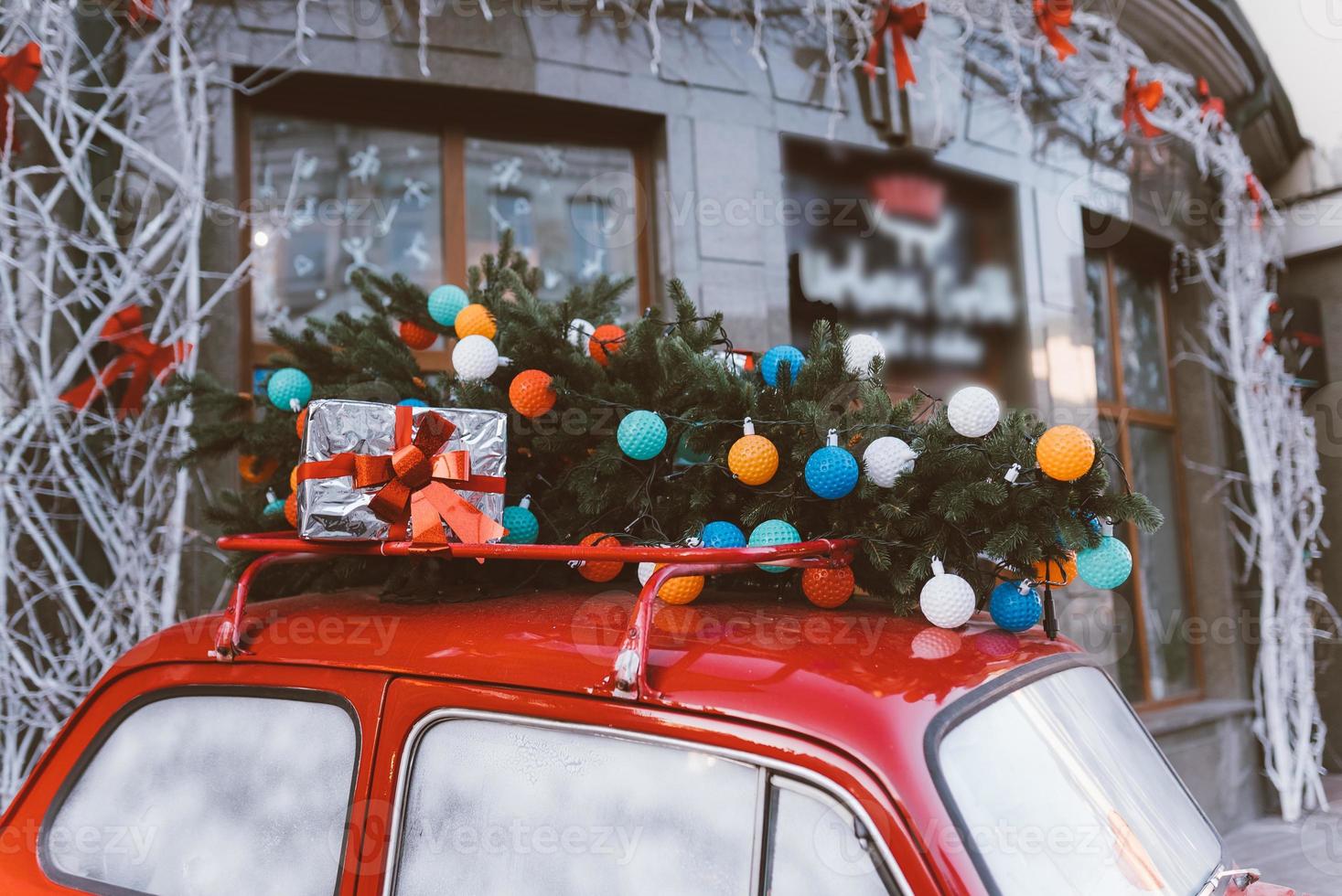 Red retro car with a Christmas tree fir tied to the roof. photo