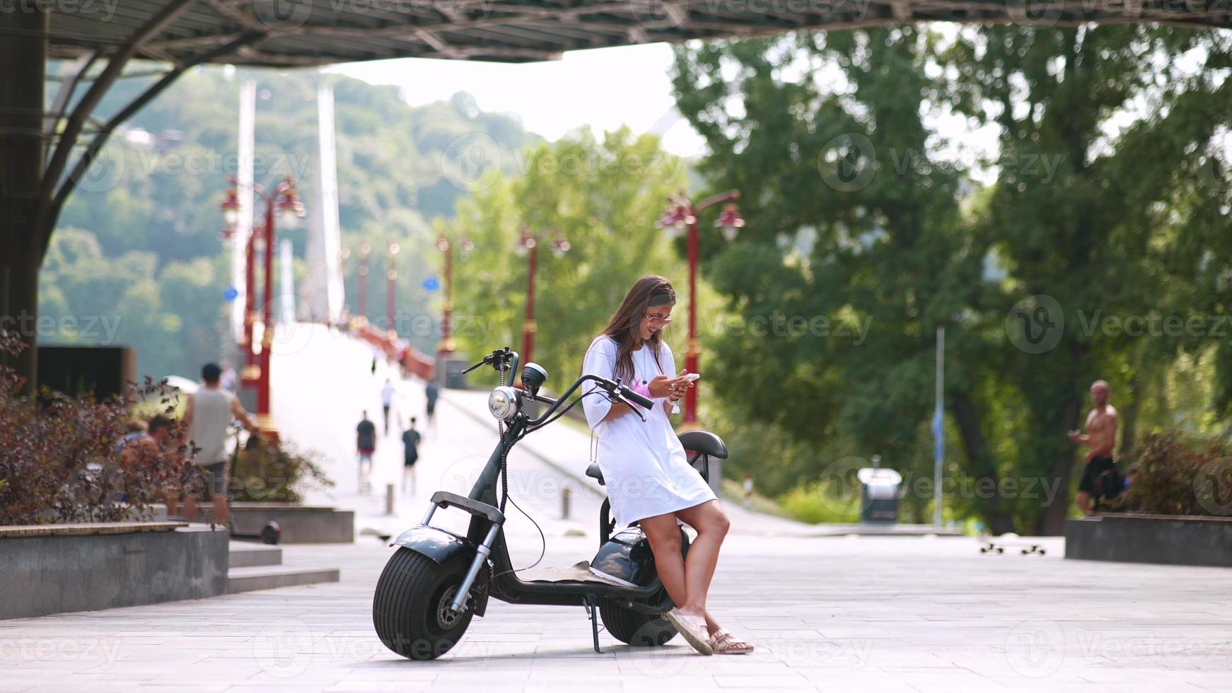 Girl sitting on a scooter and looks at smartphone photo