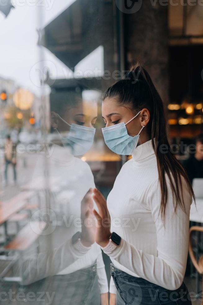 Young woman in face mask standing in front of windows in cafe. photo