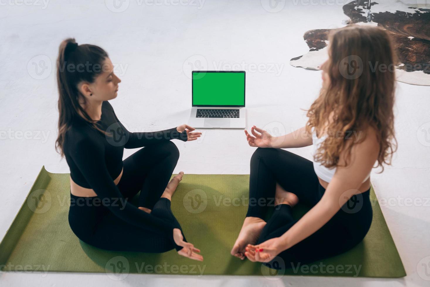 Two young women meditating in lotus pose at home photo
