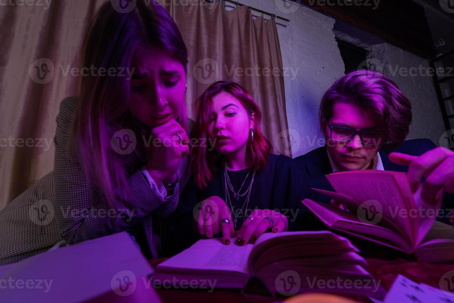 Two women and a guy are reading a mysterious books, close view photo