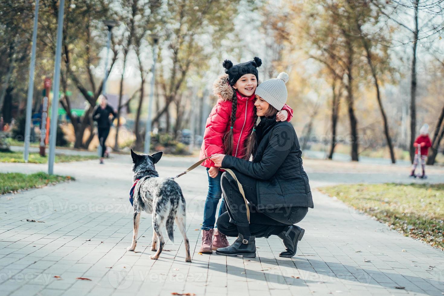 madre feliz y su hija caminan con perro en el parque de otoño foto