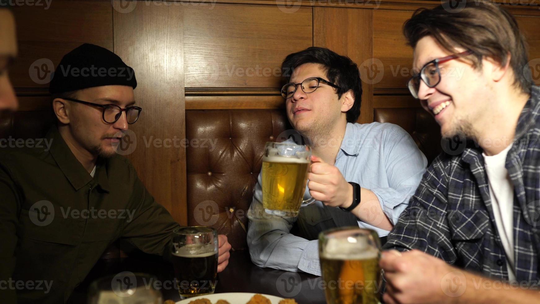 jóvenes amigos divirtiéndose juntos bebiendo cerveza y tintineando vasos en un pub. foto