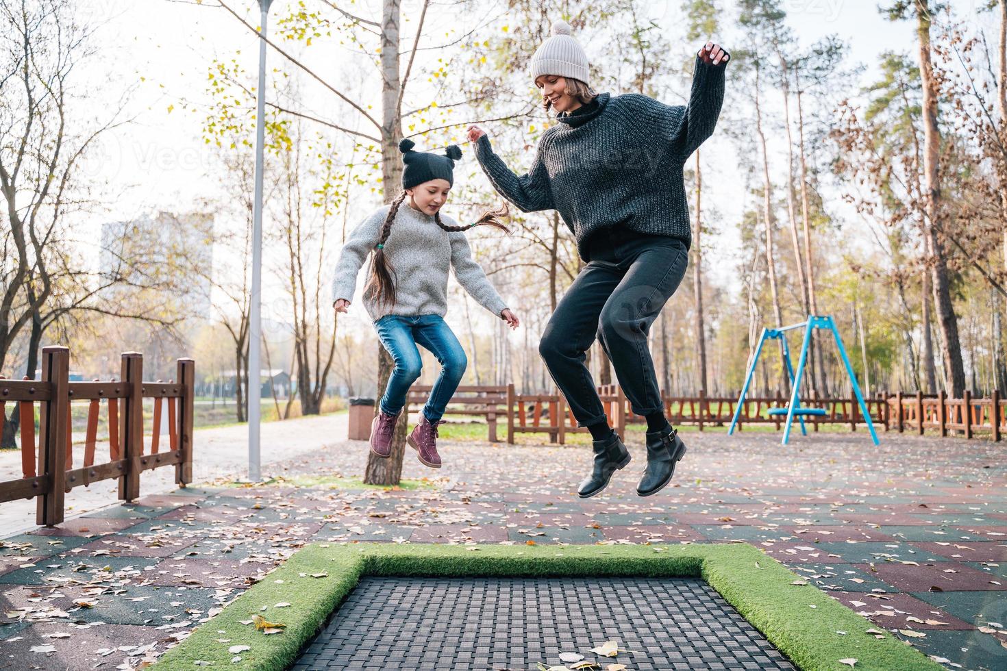 Mom and her daughter jumping together on trampoline in autumn park photo