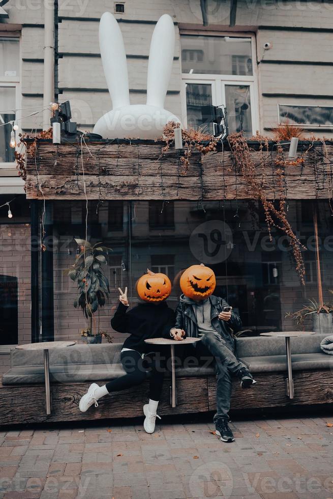 Guy and girl with pumpkin heads in a street cafe holding hands photo